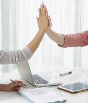 Crop hands of modern coworkers giving high five above working table with gadgets